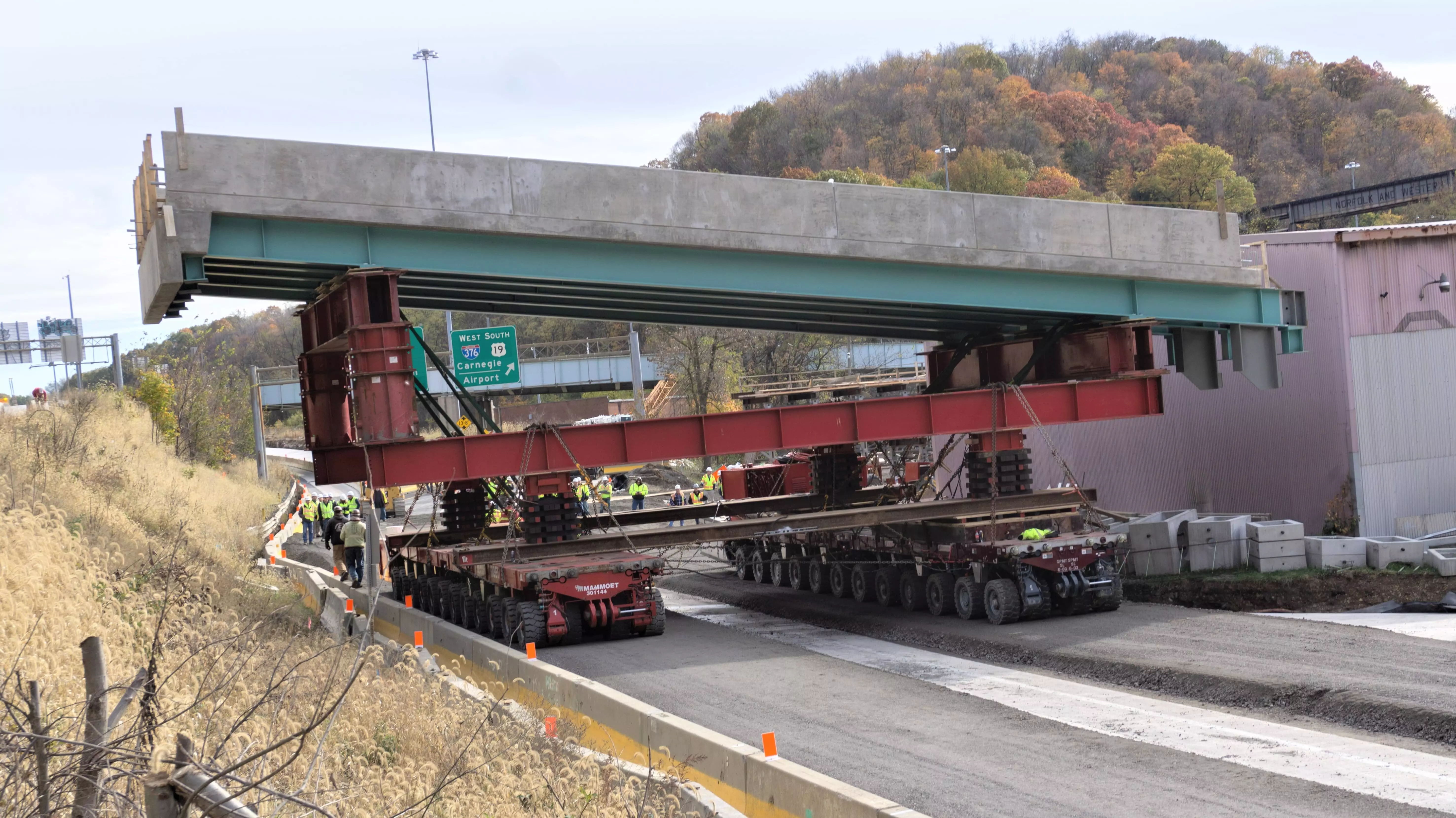 A concrete highway bridge segment is balanced atop a piece of transport equipment as wide as two lanes of traffic.